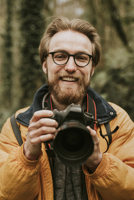 Photographer man smiling while holding camera in the woods